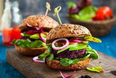 Zwei Burger mit reichlich Salatblättern, Zwiebeln, Tomaten, Patty auf einem Holzbrett angerichtet