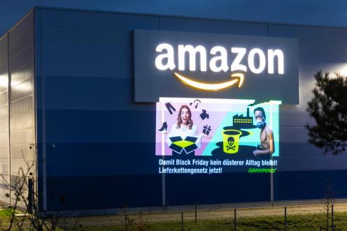 Projektion auf Gebäude: Neben dem Amazon-Logo zeigt eine Grafik den Gegensatz von Shopping aus dem Karton und Arbeitsbedingungen in einer Fabrik. Darunter steht: “Damit Black Friday kein düsterer Alltag bleibt, Lieferkettengesetz jetzt”.