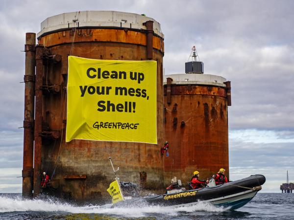 Kletterer:innen erklimmen Ölplatformen und hängen Banner mit der Aufschrift "Shell, räumt euren Dreck weg" und "Stoppt die Meeresverschmutzung" auf.